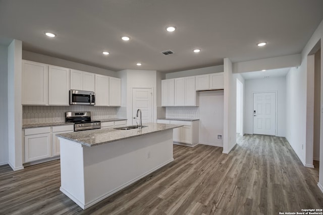 kitchen with visible vents, a sink, appliances with stainless steel finishes, white cabinetry, and a kitchen island with sink