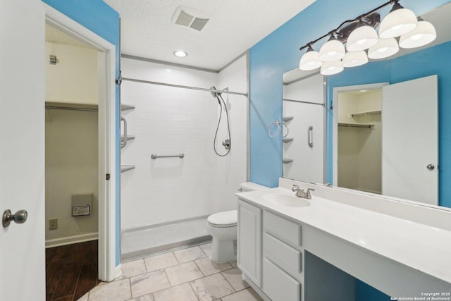 bathroom featuring visible vents, toilet, vanity, a tile shower, and a textured ceiling