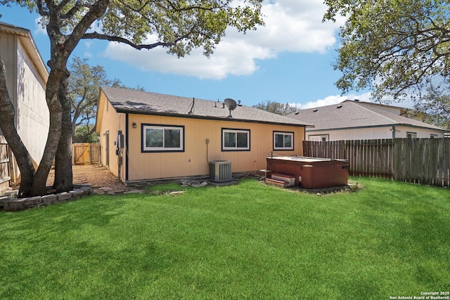 back of house featuring central air condition unit, a lawn, a hot tub, and a fenced backyard