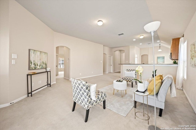 living room featuring visible vents, arched walkways, baseboards, light colored carpet, and vaulted ceiling