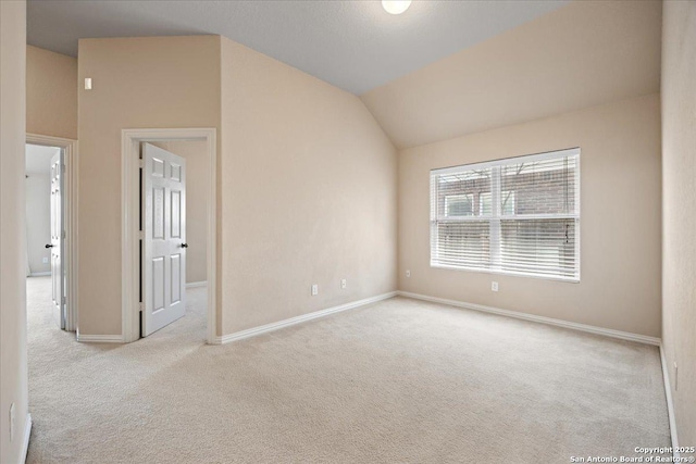 carpeted spare room featuring lofted ceiling and baseboards