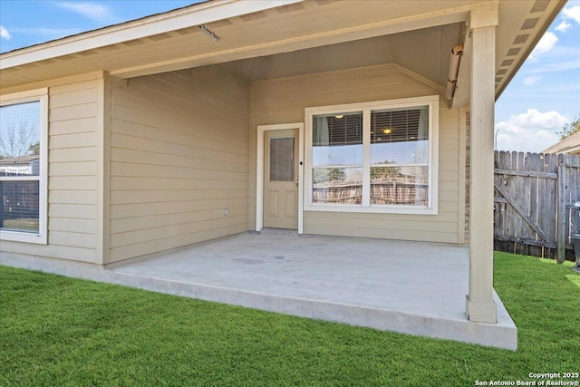 entrance to property featuring a lawn, a patio, and fence