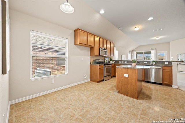 kitchen featuring brown cabinets, dark countertops, a center island, appliances with stainless steel finishes, and baseboards