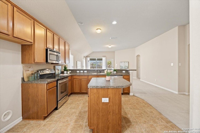 kitchen with a peninsula, arched walkways, a sink, appliances with stainless steel finishes, and a center island