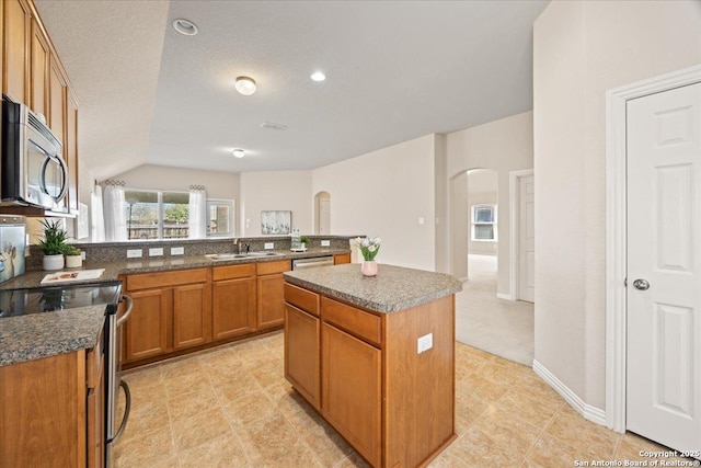 kitchen featuring a sink, a center island, arched walkways, appliances with stainless steel finishes, and brown cabinetry