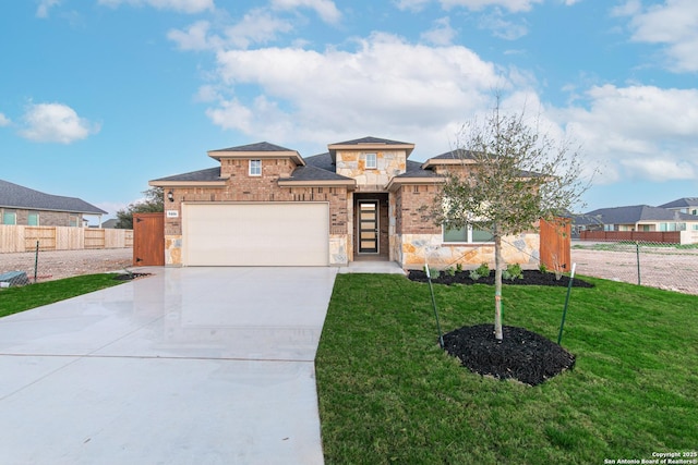 prairie-style house with a front lawn, stone siding, fence, concrete driveway, and an attached garage