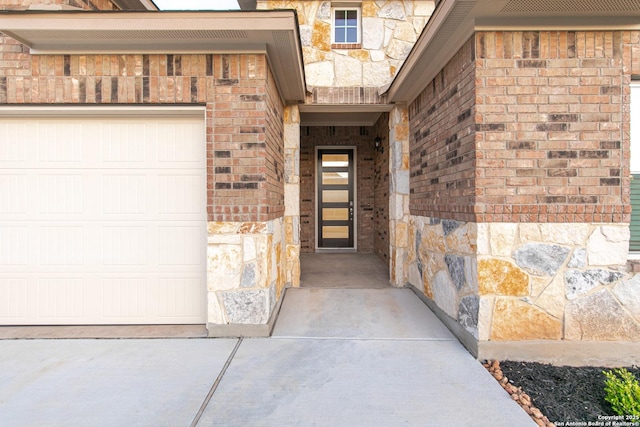 view of exterior entry with brick siding, stone siding, driveway, and a garage