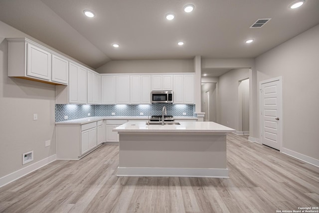 kitchen with white cabinetry, light countertops, a center island with sink, and stainless steel appliances