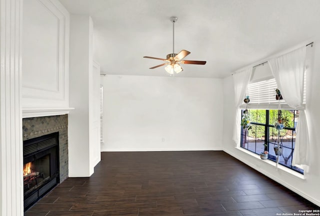 unfurnished living room with baseboards, a lit fireplace, dark wood-style floors, and a ceiling fan