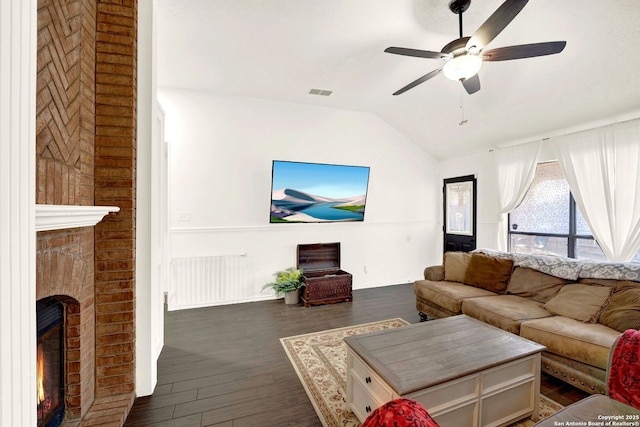 living area featuring visible vents, dark wood finished floors, vaulted ceiling, a fireplace, and a ceiling fan