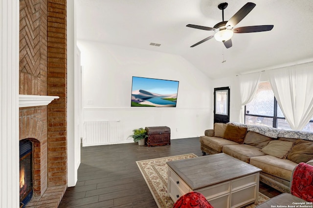 living area featuring a ceiling fan, visible vents, vaulted ceiling, dark wood-type flooring, and a brick fireplace