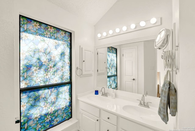 full bath with a sink, lofted ceiling, a textured ceiling, and double vanity