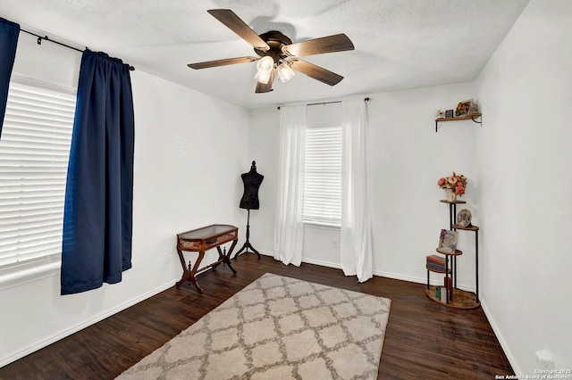 living area with dark wood-type flooring, a ceiling fan, baseboards, and a textured ceiling