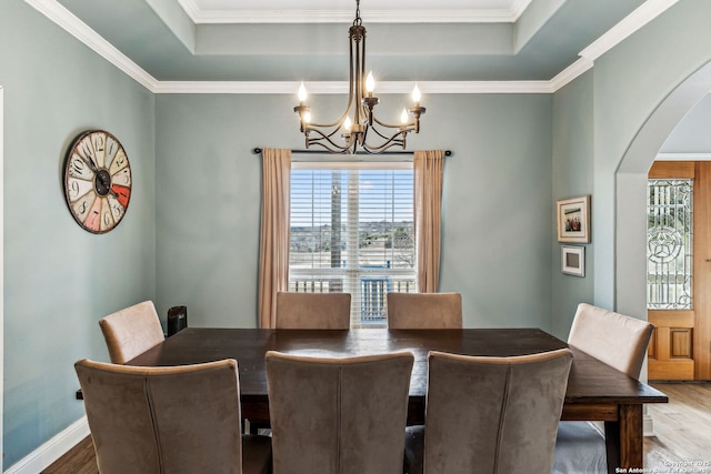 dining room with baseboards, an inviting chandelier, wood finished floors, arched walkways, and a raised ceiling