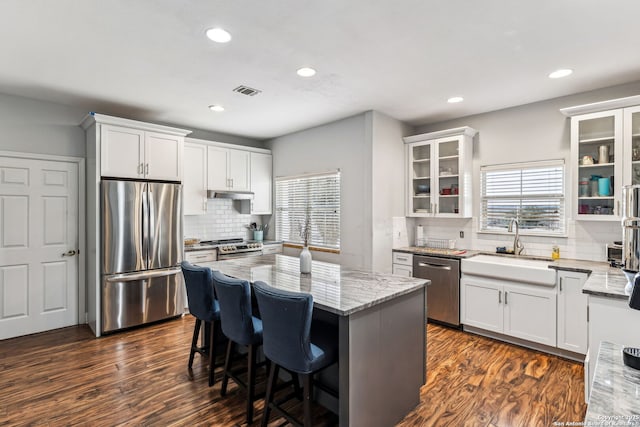 kitchen with a center island, light stone countertops, stainless steel appliances, and a sink