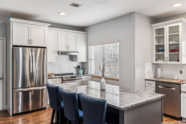 kitchen with light stone counters, dark wood-style floors, visible vents, under cabinet range hood, and appliances with stainless steel finishes