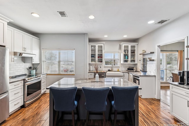 kitchen with under cabinet range hood, visible vents, appliances with stainless steel finishes, and a center island