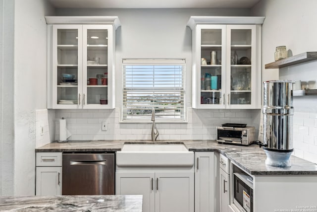 kitchen featuring dishwasher, decorative backsplash, glass insert cabinets, and a sink