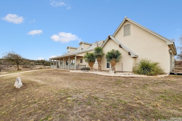 rear view of house featuring stucco siding, a yard, and covered porch