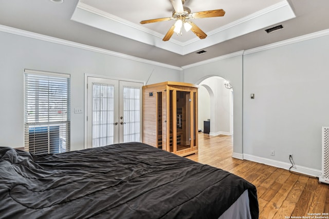 bedroom featuring a raised ceiling, wood finished floors, arched walkways, and ornamental molding