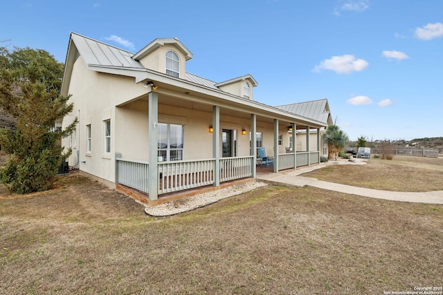 view of front of house featuring a front yard, a standing seam roof, a porch, stucco siding, and metal roof