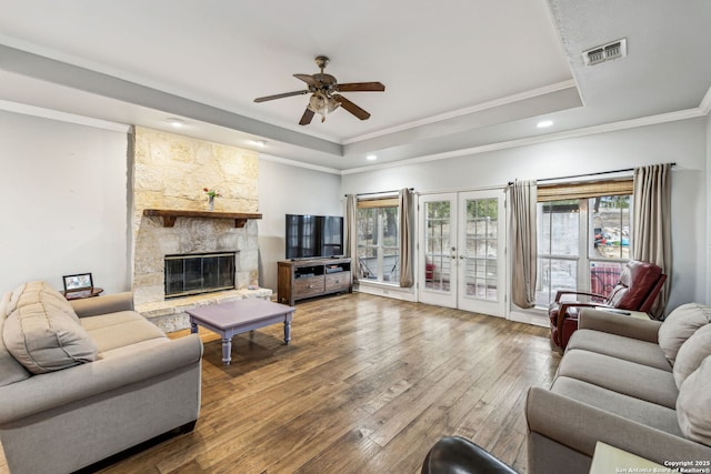 living room with a tray ceiling, visible vents, wood-type flooring, and a stone fireplace