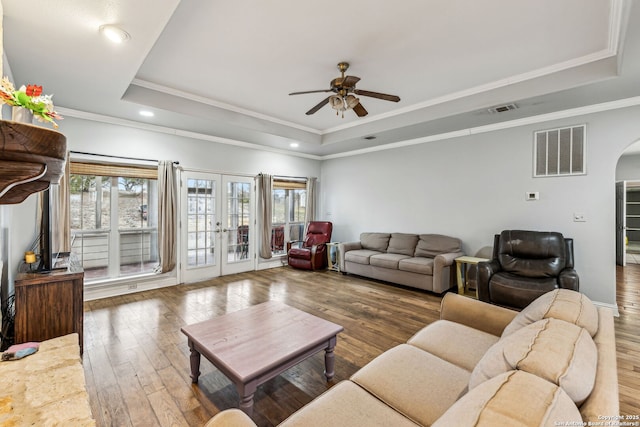 living area with a tray ceiling, arched walkways, visible vents, and french doors