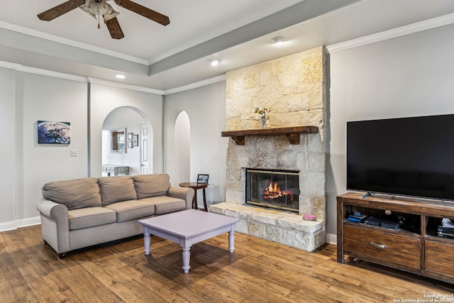 living room with hardwood / wood-style floors, a fireplace, arched walkways, crown molding, and a raised ceiling