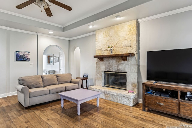 living area featuring crown molding, ceiling fan, a stone fireplace, arched walkways, and wood-type flooring