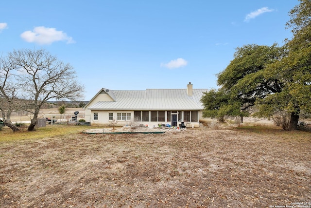 view of front of home with a standing seam roof, fence, a sunroom, metal roof, and a chimney