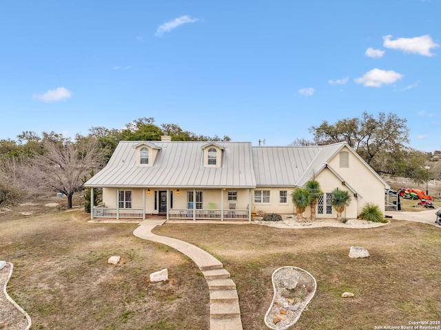 view of front facade with a standing seam roof, covered porch, a chimney, stucco siding, and metal roof