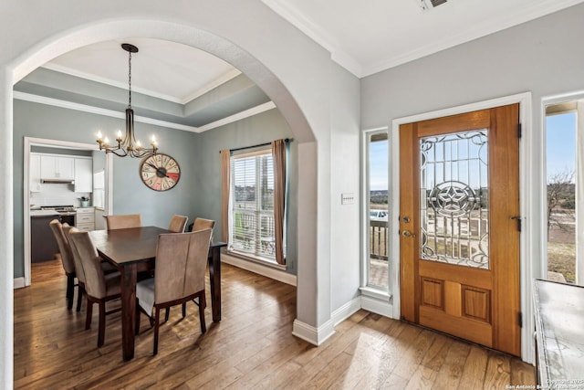 dining space with a notable chandelier, a raised ceiling, wood-type flooring, crown molding, and baseboards