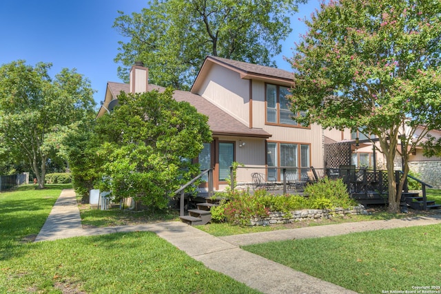 view of front of house featuring a deck, a chimney, a front yard, and a shingled roof