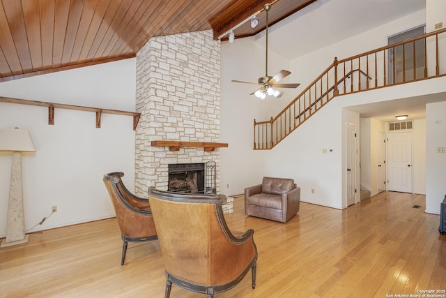 living area with a ceiling fan, a stone fireplace, beam ceiling, wood finished floors, and high vaulted ceiling