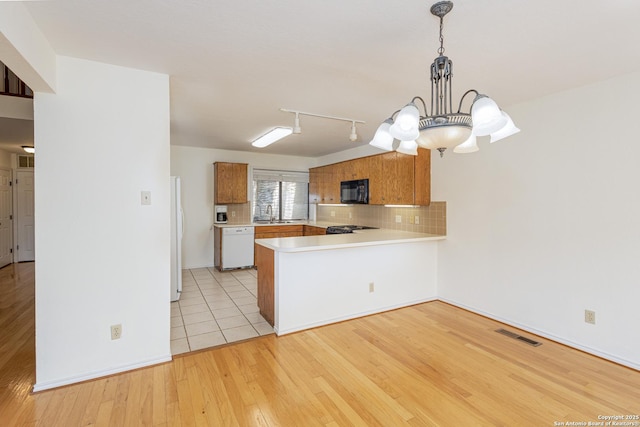 kitchen with brown cabinets, white appliances, light countertops, a peninsula, and visible vents