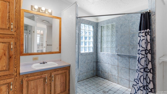 full bathroom with tiled shower, a textured ceiling, vanity, and ornamental molding