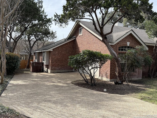 view of home's exterior with fence, a shingled roof, a chimney, concrete driveway, and brick siding