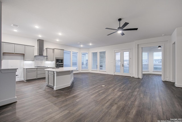 kitchen with gray cabinetry, wall chimney range hood, open floor plan, stovetop, and a sink