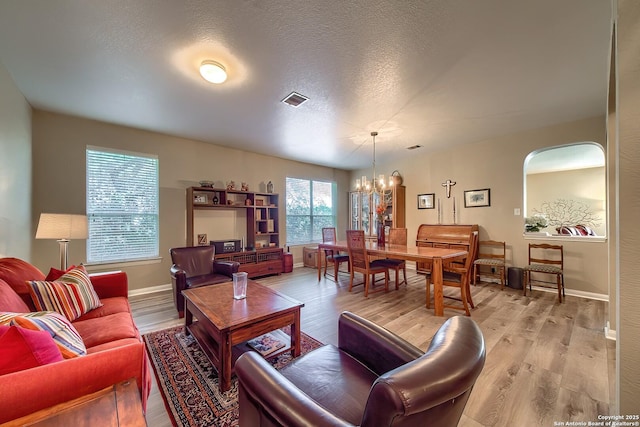 living area featuring baseboards, visible vents, a textured ceiling, a notable chandelier, and light wood-type flooring