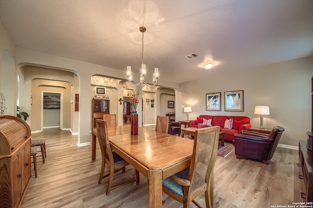 dining area featuring arched walkways, visible vents, light wood finished floors, and a notable chandelier