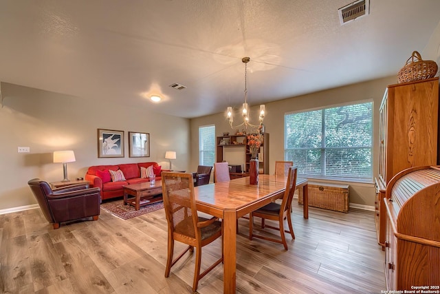 dining space featuring an inviting chandelier, baseboards, visible vents, and light wood finished floors