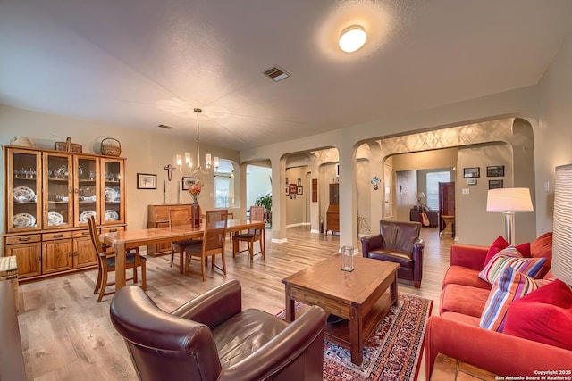 living area featuring arched walkways, visible vents, light wood-type flooring, and an inviting chandelier