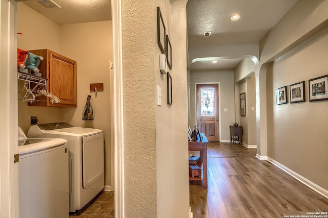 clothes washing area with wood finished floors, cabinet space, arched walkways, separate washer and dryer, and baseboards