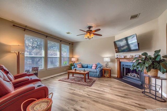 living room featuring visible vents, a textured ceiling, a fireplace with flush hearth, and wood finished floors