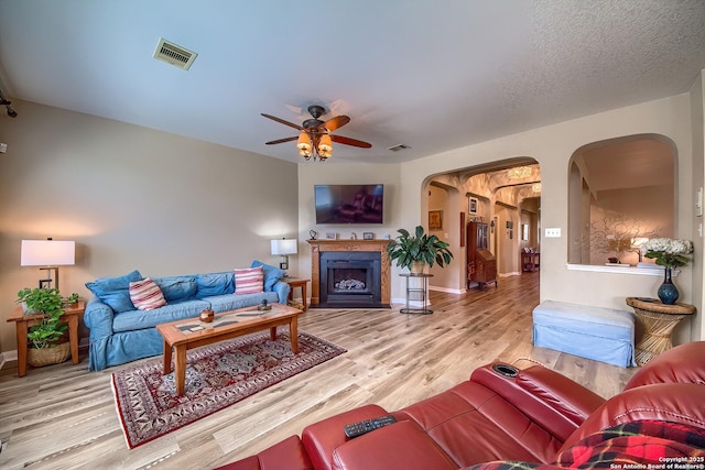 living room featuring visible vents, a fireplace with flush hearth, wood finished floors, and a ceiling fan