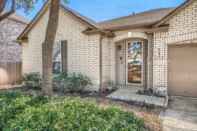 entrance to property featuring brick siding, fence, a garage, and a shingled roof