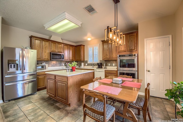 kitchen featuring tasteful backsplash, visible vents, a kitchen island, brown cabinets, and appliances with stainless steel finishes