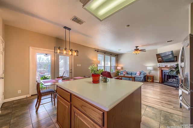 kitchen with visible vents, a center island, a fireplace, freestanding refrigerator, and brown cabinetry