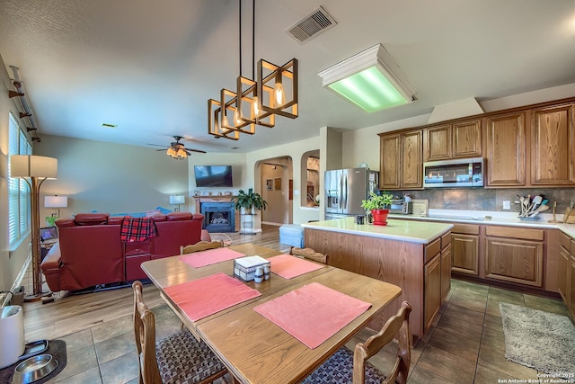 kitchen featuring visible vents, a fireplace with raised hearth, backsplash, stainless steel appliances, and brown cabinetry