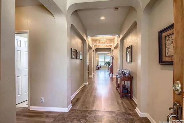 corridor with arched walkways, visible vents, stone finish floor, and baseboards